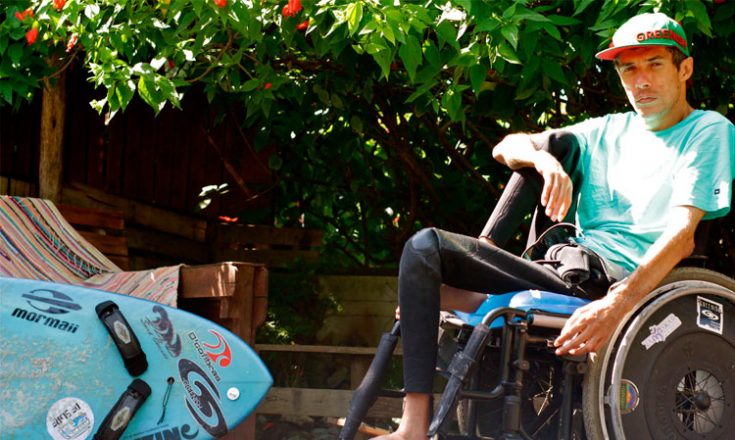 Rapaz em uma cadeira de rodas em frente a uma prancha de surf