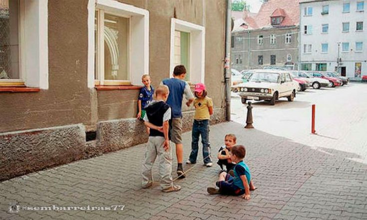 Várias crianças brincam na calçada de uma rua