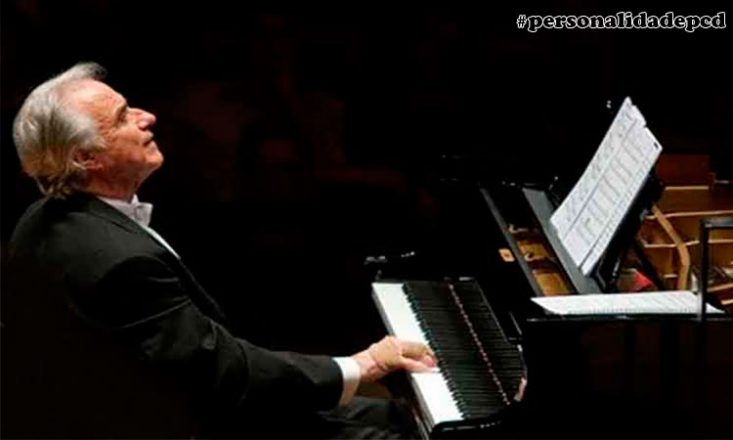 Foto horizontal, escura, de um homem de meia idade, vestindo um fraque preto, de lado, tocando piano. No alto, à direita, o sinal de hashtag e as palavras personalidadepcd