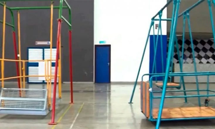 Foto de um ginásio escolar com dois brinquedos adaptados para crianças cadeirantes.